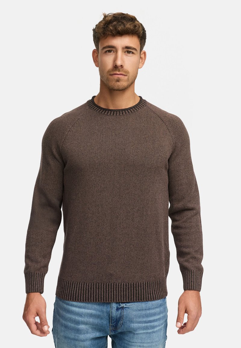 Pull en maille marron avec un col et un ourlet côtelés, présentant un tissage texturé et des manches raglan. Porté avec un jean en denim bleu.
