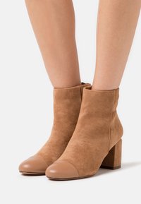 Bottines en daim couleur beige avec un bout rond en cuir lisse et un talon carré. Les bottines sont munies d'une fermeture éclair à l'arrière.
