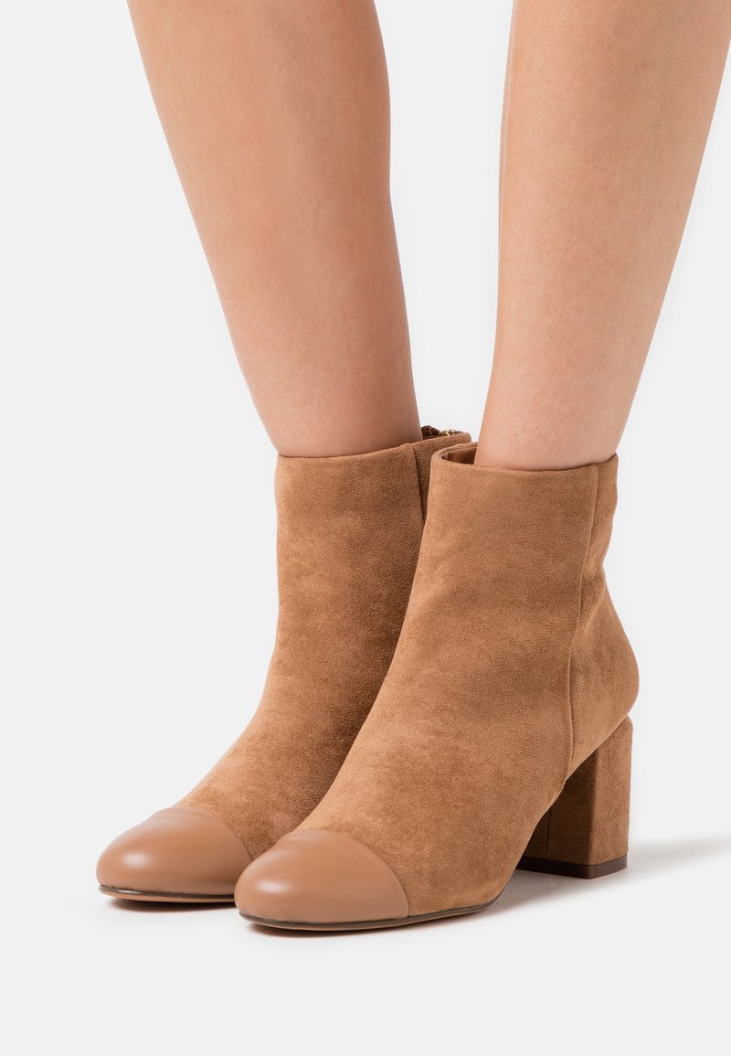 Bottines en daim couleur beige avec un bout rond en cuir lisse et un talon carré. Les bottines sont munies d'une fermeture éclair à l'arrière.