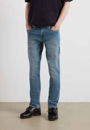 Jasnoniebieskie dżinsy z denimu z wyblakłym wzorem, prostymi nogawkami, pięcioma kieszeniami, zestawione z czarnymi sznurowanymi butami.