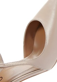 Chaussure à talon haut en cuir beige à bout pointu, finition lisse et coutures visibles le long des bords.