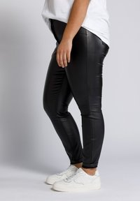 Zwarte neplederen broek met een slim fit, met een gladde textuur en zijnaad, gecombineerd met witte sneakers.