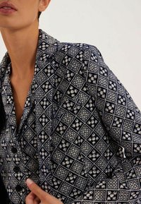 Chemise bleu marine à boutons, ornée d'un motif floral géométrique blanc, avec un tissu texturé et un col ajusté.