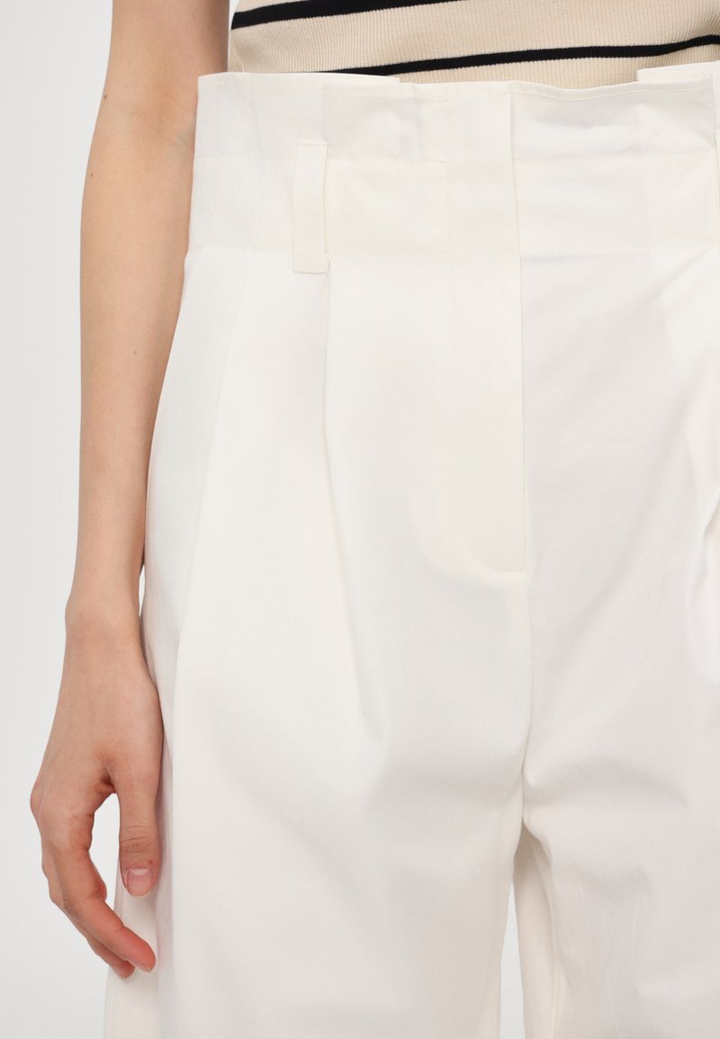 White high-waisted trousers in lightweight fabric, featuring pleats, a flat waistband with a belt loop, and a smooth texture.