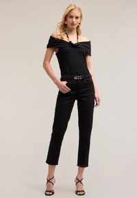 Top negro sin mangas combinado con pantalones ajustados negros y tacones de tiras negros. Incluye un cinturón decorativo y un collar voluminoso.