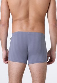 Pantaloni da bagno grigi realizzati in tessuto liscio ed elastico, con una vita senza cuciture e una sottile texture verticale.