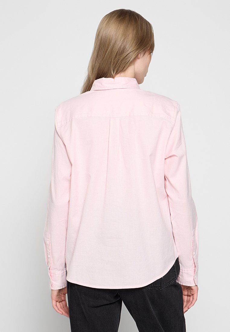 Camisa de manga larga rosa claro con cuello abotonado, ajuste relajado, detalle en la yugo trasera y puños abotonados, hecha de suave tela de algodón.