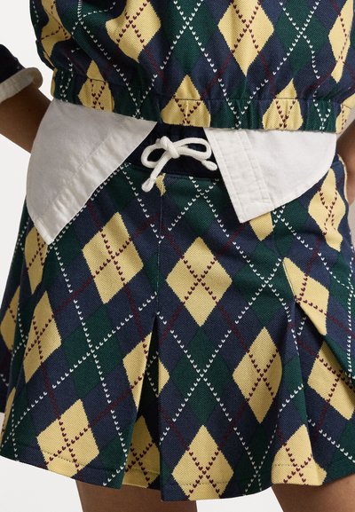 Mintás szoknya gyémánt mintával zöld, sárga és sötétkék színekben. Fehér derékrésszel rendelkezik, amely zsinórral állítható, és pliszékkel van díszítve.