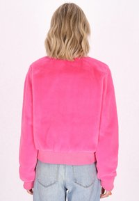 Giacca rosa fluffy con un design cropped, maniche e orlo a coste, texture morbida e retro semplice. Abbinata a jeans blu chiaro.