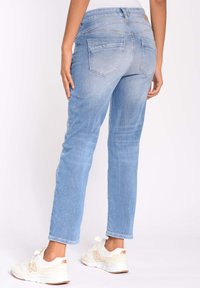 Jeans de mezclilla azul claro con un corte recto, dos bolsillos traseros y una textura sutilmente deslavada, combinados con zapatillas blancas.