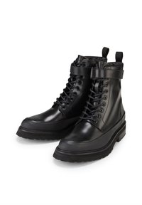 Botas de cuero negro hasta el tobillo con cordones y hebilla. Presentan un acabado suave, punta redondeada y una suela de goma gruesa. Dos tiradores en la parte superior.