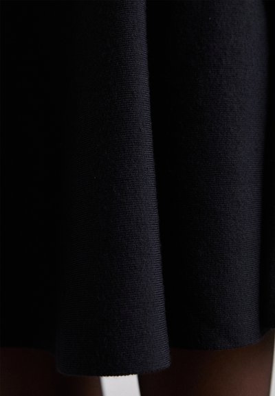 Tejido de vestido de punto negro con una superficie texturizada y un dobladillo ligeramente acampanado. El material parece suave y denso.