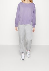 Lila sweatshirt med långa ärmar, bred halsringning; kombinerad med ljusgrå mjukisbyxor med avslappnad passform; vita sneakers med röda accenter.