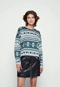 Suéter verde e branco com padrão, decote redondo, mangas longas e um corte descontraído, combinado com uma saia mini preta de couro com zíperes.