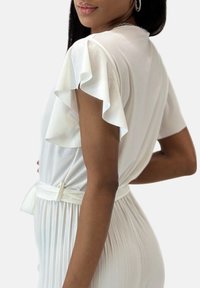 Top bianco con maniche corte a volant, tessuto liscio, vita arricciata e gonna plissettata. Design minimalista, versatile per varie occasioni.