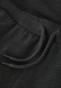 Temno siva tkanina trenirke s rebrastim pasom. Ima izvlečne vrvice s plastičnimi konicami in gladko teksturo.