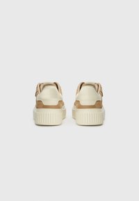Baskets beige et crème avec une tige en suède et cuir, un col rembourré et une semelle épaisse et texturée. Présente un logo minimaliste à l'arrière.