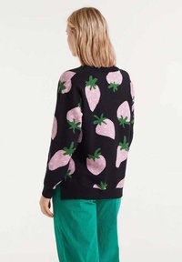 Suéter negro con un patrón repetido de fresas rosas con hojas verdes. Textura de punto, corte relajado y dobladillo acanalado.