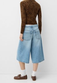 Džínové culottes v světle modré barvě s uvolněným střihem, mají zadní kapsy a třepící se lem. V kombinaci s hnědým dlouhým rukávem s puntíky a hnědými botami.