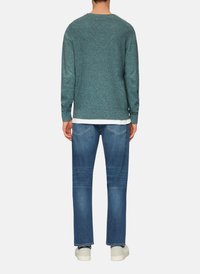 Pull en teinte sarcelle texturé à manches longues, associé à un jean bleu à jambe droite. Le mannequin porte des baskets blanches. Une chemise superposée visible en dessous.