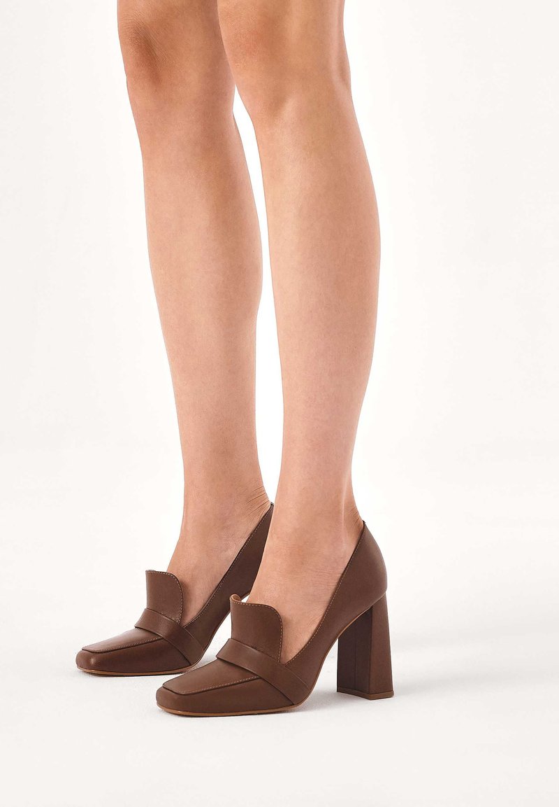 Rjavi usnjeni čevlji z visoko peto, kvadratnim sprednjim delom in širokim trakom za poudarek. Blokasta peta je teksturirana z gladkim zaključkom.