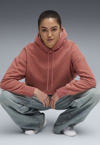 Krótkie hoodie z mieszanki bawełny w odcieniu przykurzonego różu, z teksturowanym materiałem, kapturem ze sznurkiem i subtelnym logo. W zestawie z szerokimi spodniami dżinsowymi w jasnym odcieniu.