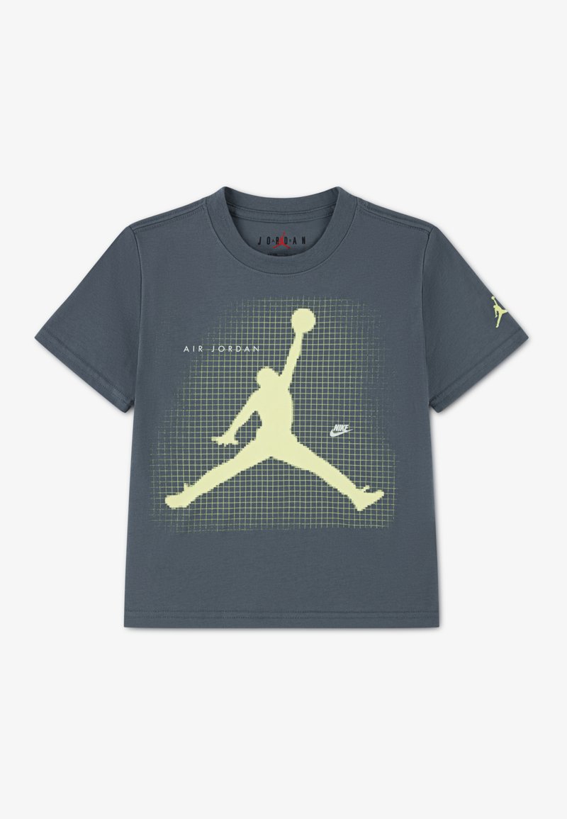 Γκρι μπλουζάκι με κοντά μανίκια που διαθέτει μεγάλο κίτρινο λογότυπο Jumpman, φόντο με μοτίβο πλέγματος και το κείμενο "AIR JORDAN" σε λευκό.