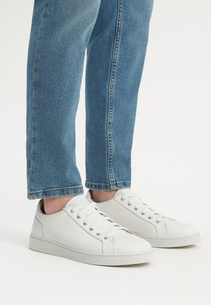 Białe skórzane sneakersy z perforowanym wzorem, okrągłym noskiem i płaską gumową podeszwą. Widoczne sznurówki i metalowe oczka to charakterystyczne cechy.