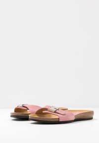 Ett par rosa mocka slidesandaler med korkfotsulor och silverfärgade spännen på en vit yta.