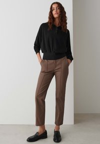 Zwarte henley-stijl sweatshirt met een relaxte pasvorm, gedragen met taps toelopende bruine broek met voornaad, die zwarte instap schoenen aanvult.