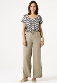 Losse, lichtbeige linnen broek met een trekkoord in de taille, gecombineerd met een zwart-wit patroon top met korte mouwen.