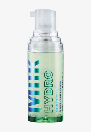 Petit flacon pompe vert translucide étiqueté "Milk Hydro Grip Primer Base Adhérente", contenant 10 ml de produit cosmétique liquide.