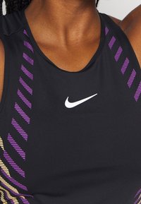 Top atlético negro sin mangas con rayas diagonales en morado y amarillo en un lado, que presenta un logo blanco de Nike en la parte frontal. Textura suave.