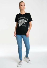 Black cotton t-shirt featuring a gray graphic of a wolf and the text "Winter is Coming" from Game of Thrones. Crew neck, short sleeves.