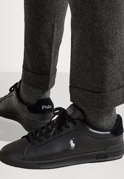 Mustad nahast tossud valge Polo logo ja hobuse embleemiga, ümmarguste šnööridega ja tekstuuriga tallaga, koos hallide pükstega.