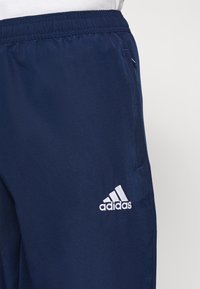 Navy treningsbukser i glatt stoff har en elastisk midje, sidelommer og en hvit brodert logo på venstre lår.