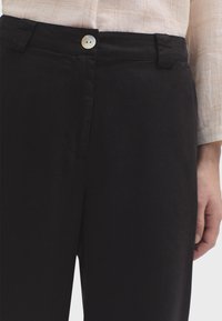 Schwarze Hosen aus glattem Stoff, mit einem vorderen Knopfverschluss und Gürtelschlaufen, in lockerer Passform und minimalistischem Design.