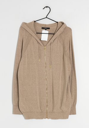Hellbrauner Kapuzenpullover mit Reißverschluss, Kapuze, Kordelzügen und gerippten Details an den Ärmeln, der an einem schwarzen Kleiderbügel mit einem weißen Preisschild hängt.