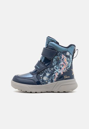 Botas de tobillo azul marino con dos correas de velcro, material brillante, con un estampado de personajes y acentos de copos de nieve en el costado. Suela blanca.