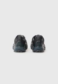 Ein Paar dunkelgraue Sportschuhe, von hinten gezeigt, mit strukturierten Zwischensohlen und Zuglaschen auf einem schlichten hellen Hintergrund.