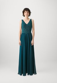 Duga teal haljina s V-izrezom i složenim beaded gornjim dijelom. Proljetna chiffon suknja, bez rukava, i suptilna A-linija silueta.