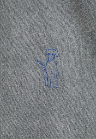 Dessin à la ligne bleue d'un chien assis brodé sur un fond de tissu gris.