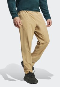 Beige Wanderschuhe mit einem elastischen Bund, seitlichen Taschen und einer lockeren Passform, kombiniert mit schwarzen Sportschuhen.