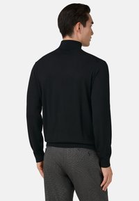 Černý rolák vyrobený z hladké tkaniny, se siluetou s přiléhavým střihem a žebrovanými manžetami. Nosený s kostkovanými šedými kalhotami.