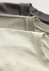 Drei gefaltete Rundhals-T-Shirts in Hellgrau, Olivgrün und Dunkelgrau, übereinander gestapelt auf hellem Hintergrund.