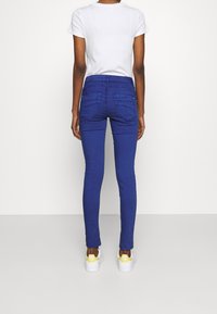 Färgglada blå denimjeans med normal hög midja, bakfickor och en slät yta, kombinerade med vita sneakers med gula detaljer.