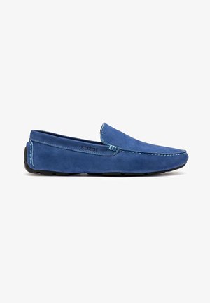 Chaussure à enfiler en daim bleu avec coutures contrastées, bout arrondi et semelle en caoutchouc noire, présentant un design minimaliste.