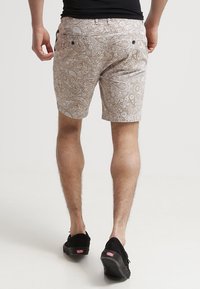Shorts beige clair avec un motif paisley blanc complexe, deux poches arrière, et devant plat, fabriqués en tissu respirant.