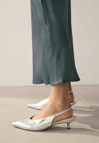 Silberne Slingback-High Heels mit spitzer Zehenpartie und rissiger Textur. Niedriger Kittenheel und eine glatte, abgerundete Rückseite für einen sicheren Sitz.