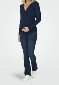 Top de manga larga de canalé en color navy con escote en V y bordes de encaje, combinado con jeans azul oscuro y zapatillas blancas, resaltando un estilo casual.